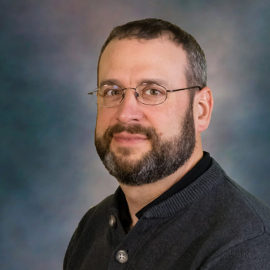 Head-and-shoulders portrait of a man with glasses and a beard, wearing a dark sweater.