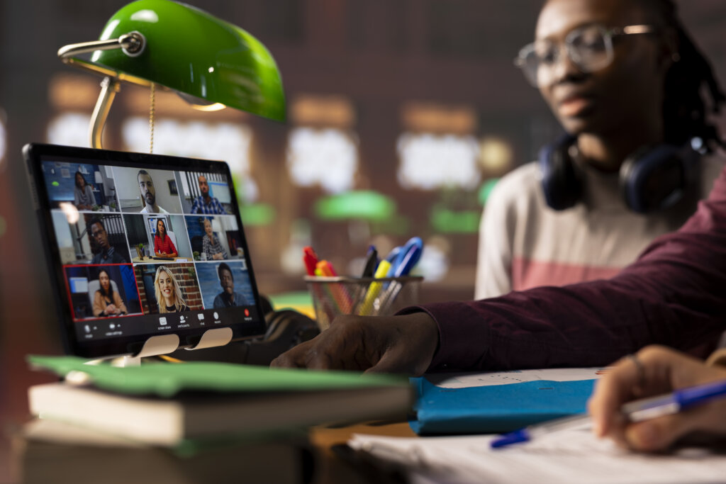 Student on video call during bolted joint training, taking notes at desk with lamp and headphones.